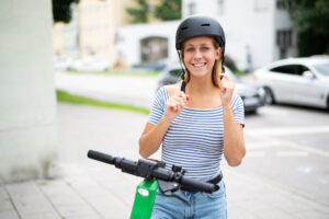 Junge Frau zieht einen Helm an um mit einem E-Scooter zu fahren