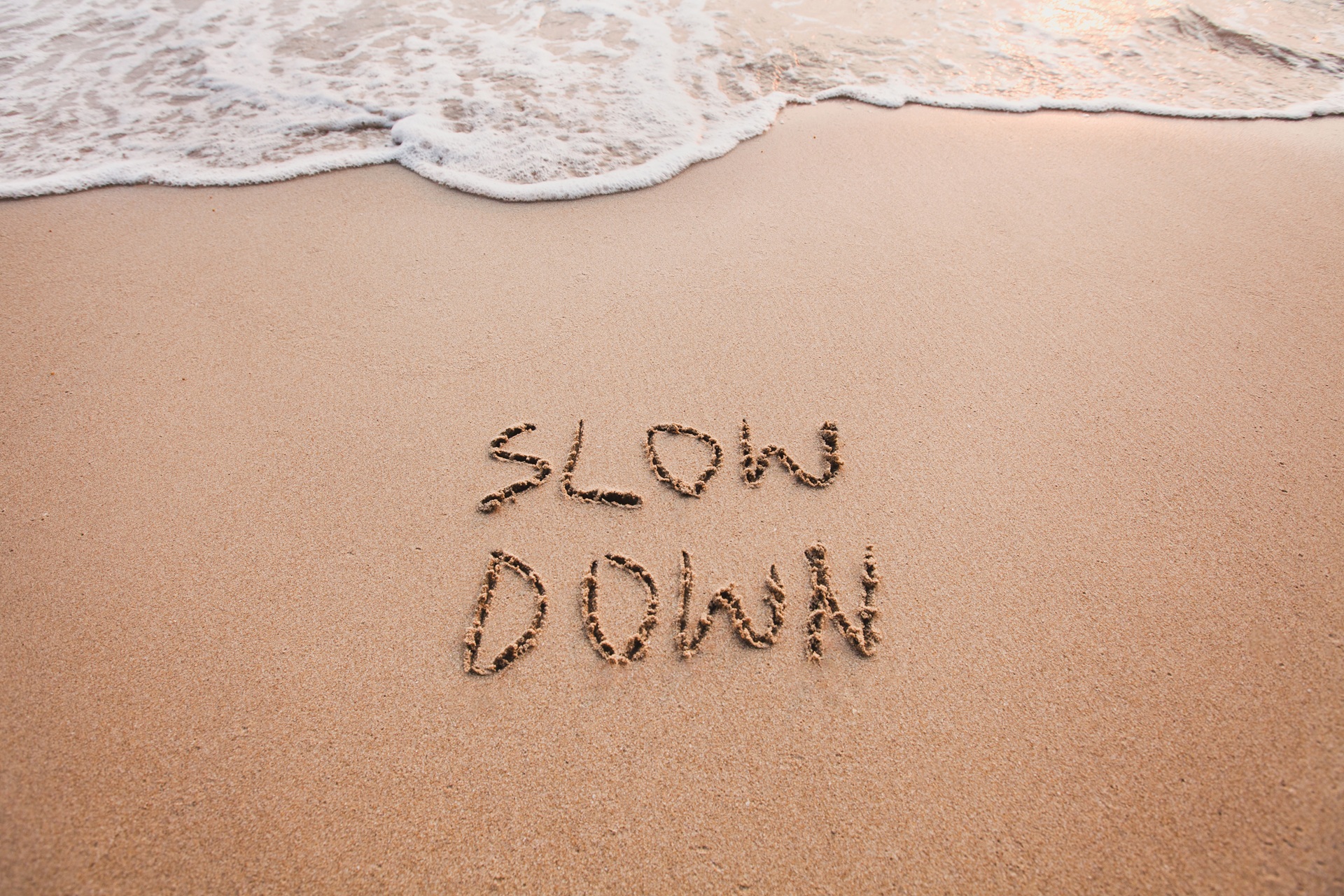 Schriftzug Slow Down im Sand am Strand | Elfa Master